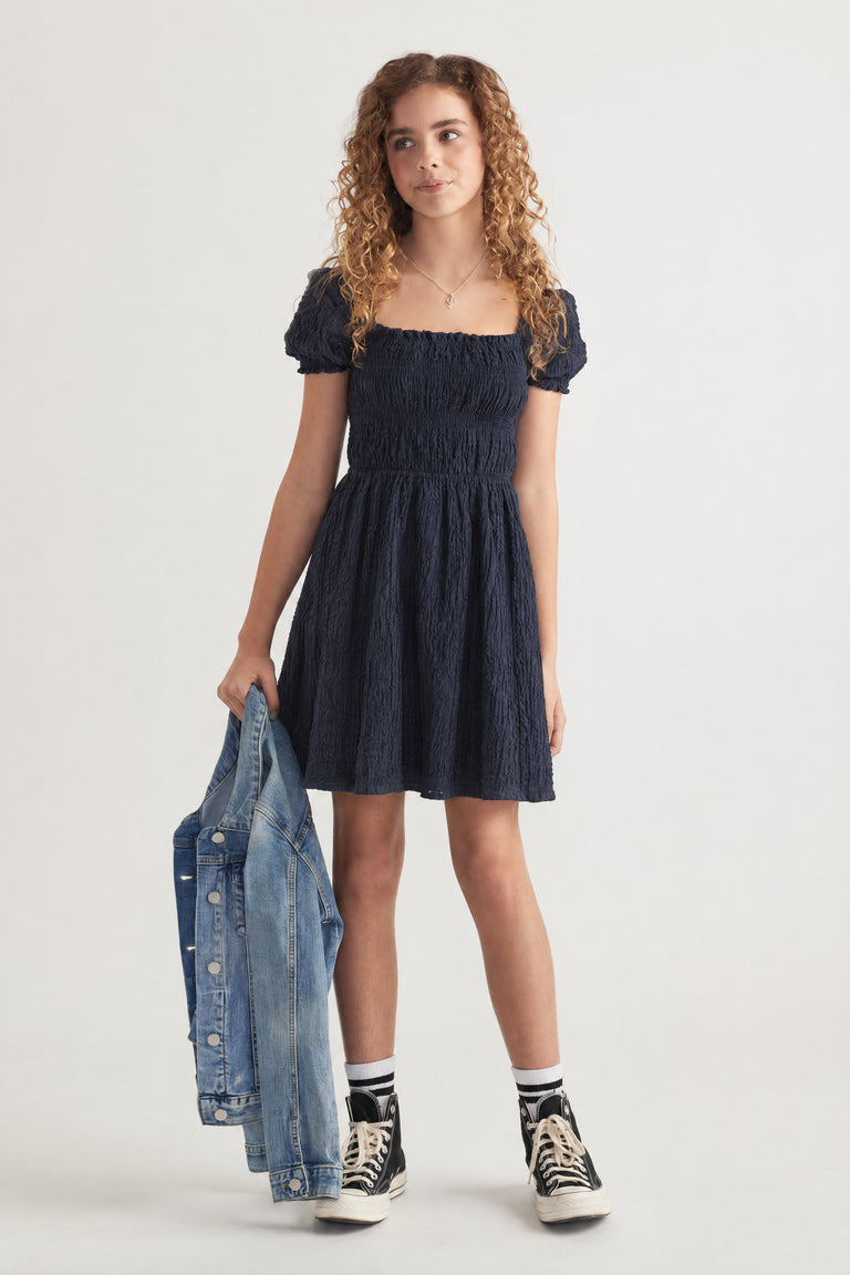 Girl wearing a navy textured mini dress with puff sleeves, denim jacket and high top sneakers