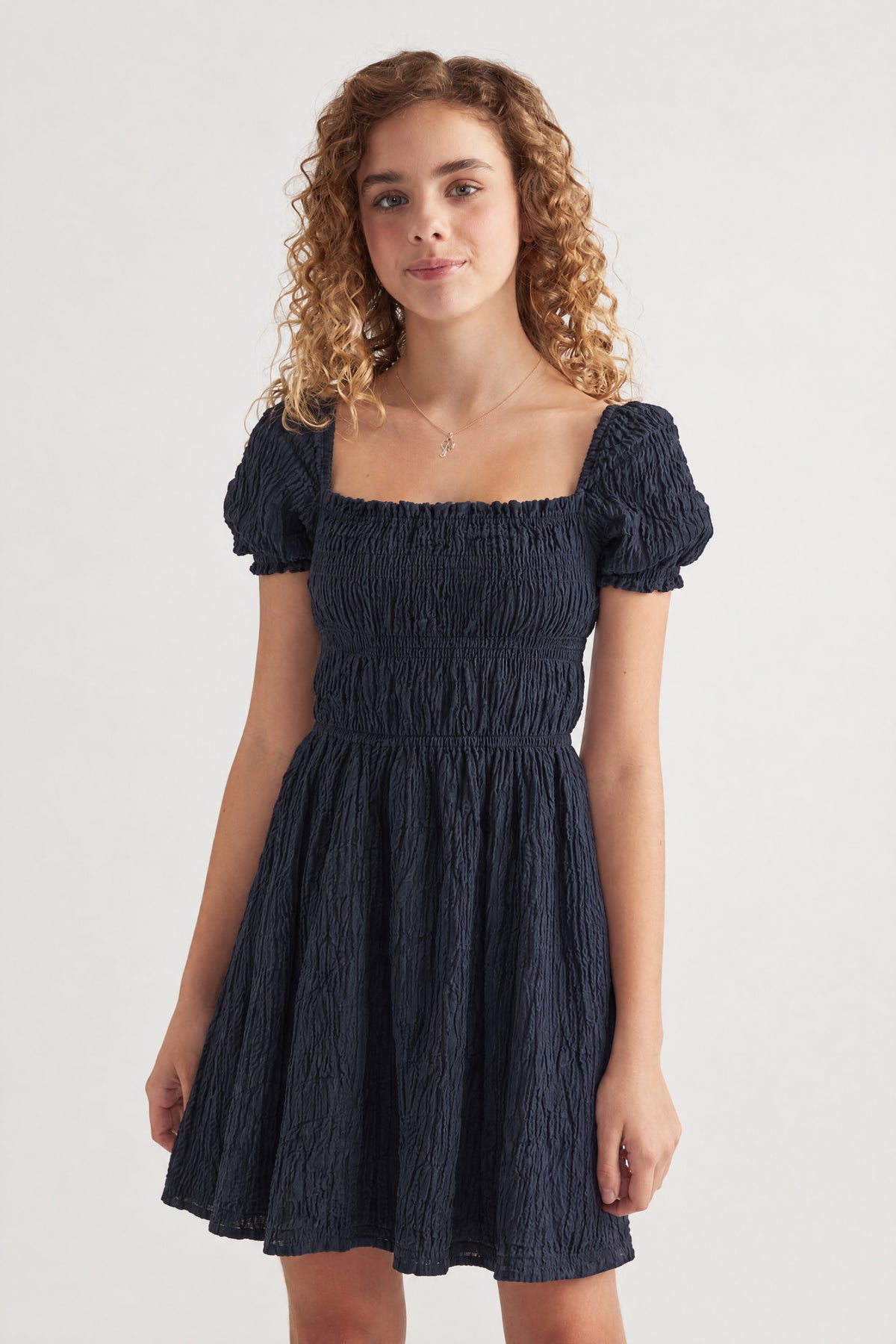 Girl wearing a navy textured mini dress with a square neckline puff sleeves and tiered skirt