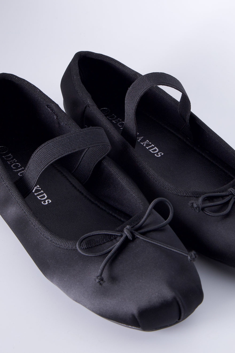 Pair of black satin ballet flats for girls with elastic straps and delicate bow detailing on toes