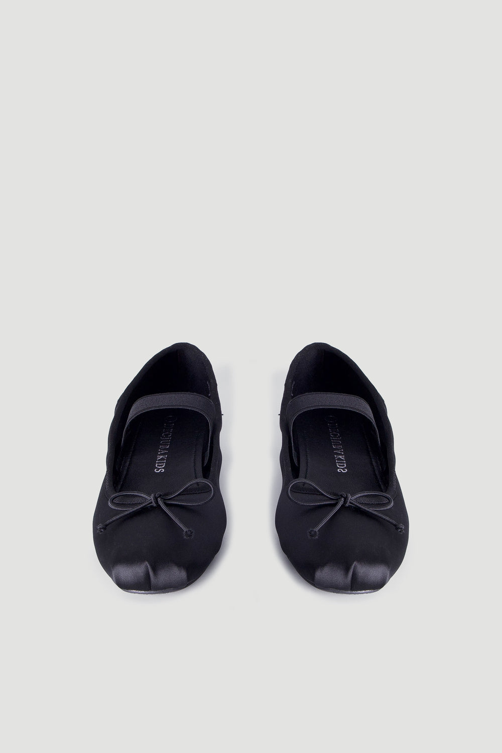 Pair of black satin ballet flats for girls featuring a delicate bow and a supportive elastic strap