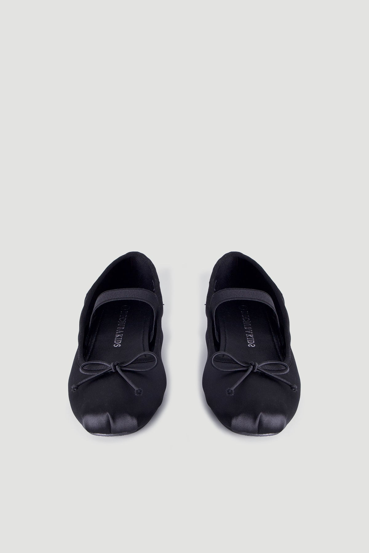 Pair of black satin ballet flats for girls featuring a delicate bow and a supportive elastic strap