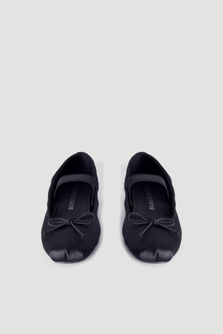 Pair of black satin ballet flats for girls featuring a delicate bow and a supportive elastic strap