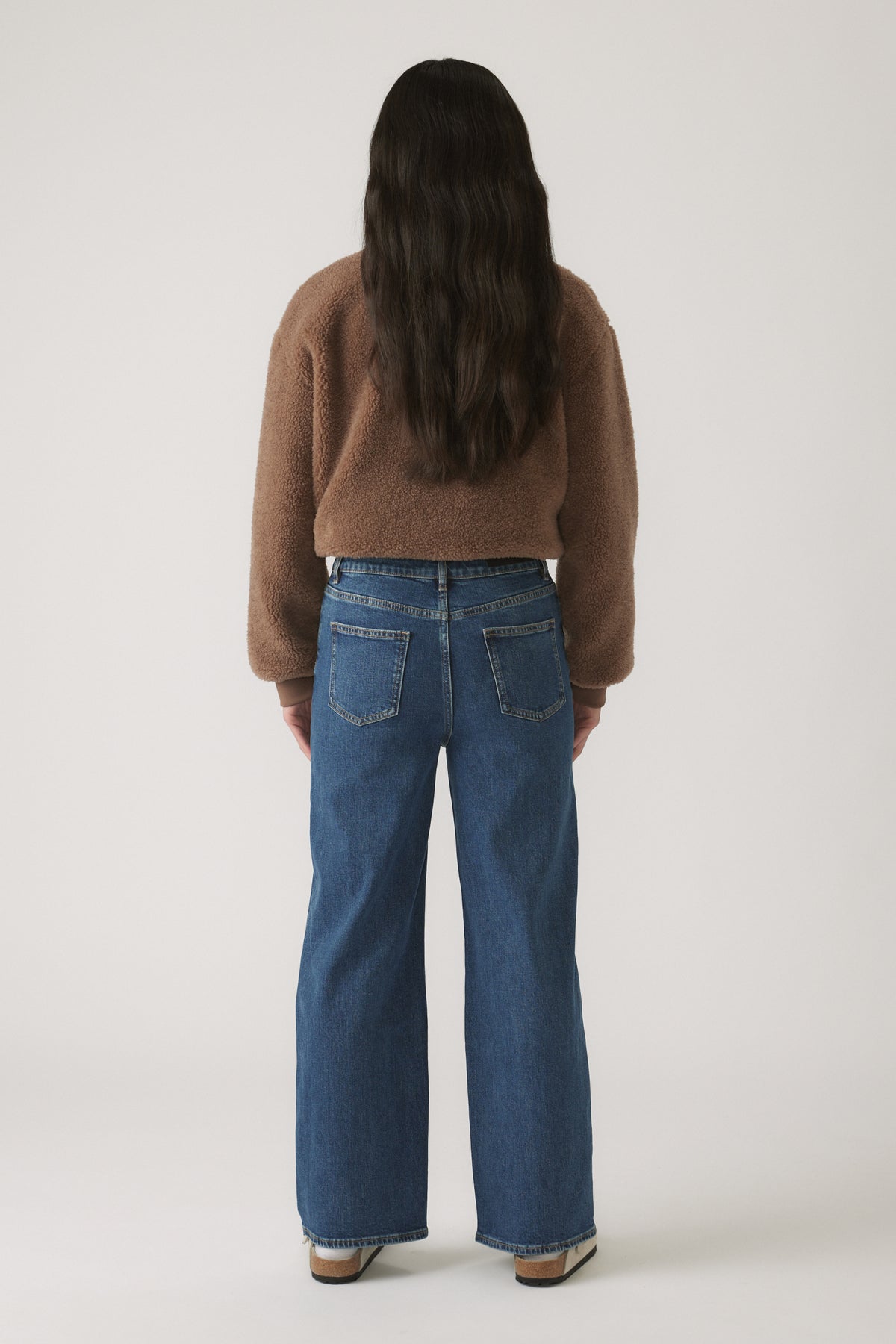 Back view of girl wearing relaxed fit blue denim jeans paired with a cozy brown textured sweater.