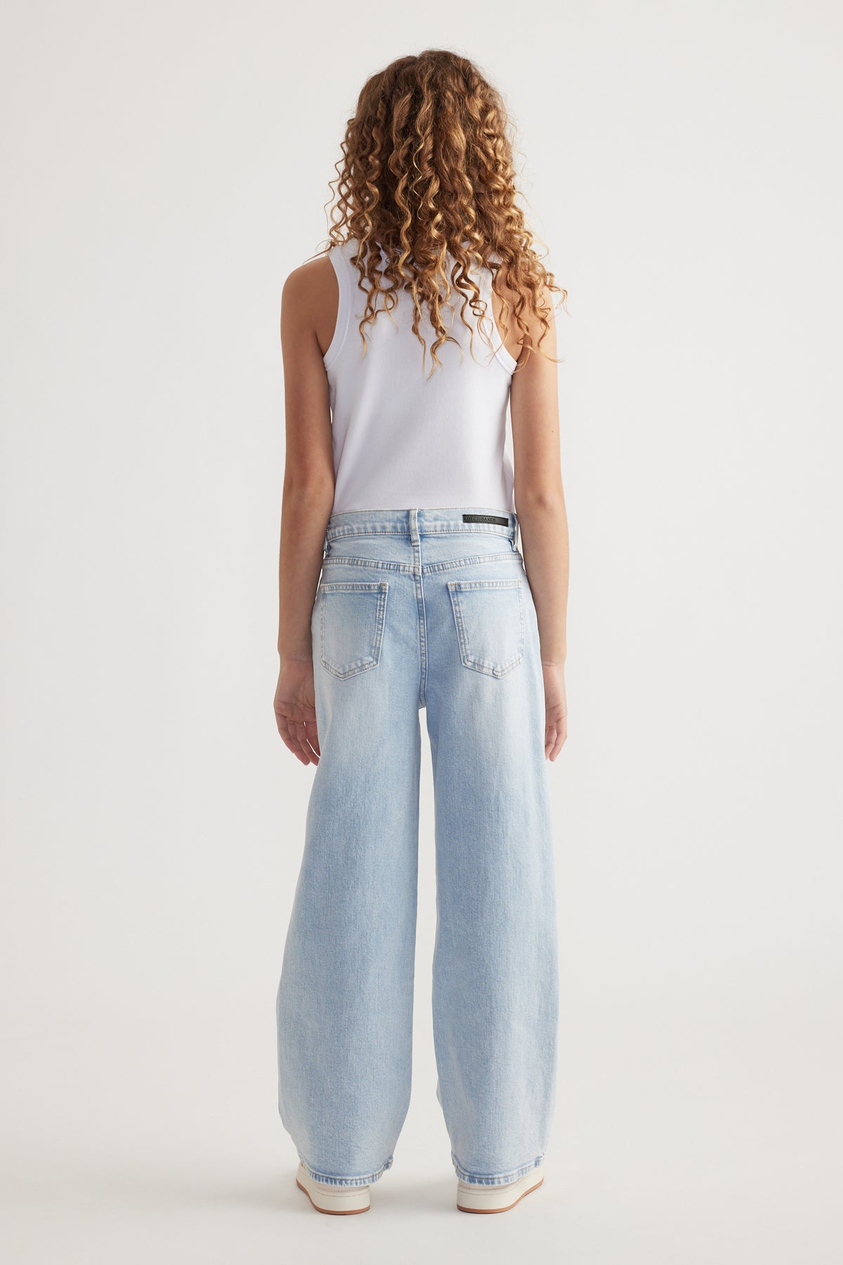 Rear view of girl wearing relaxed fit light blue mid-rise wide leg jeans with functional pockets and white tank top