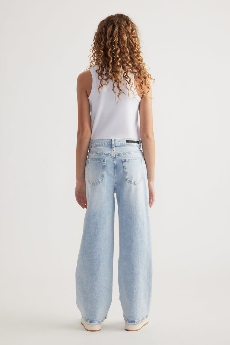 Rear view of girl wearing relaxed fit light blue mid-rise wide leg jeans with functional pockets and white tank top