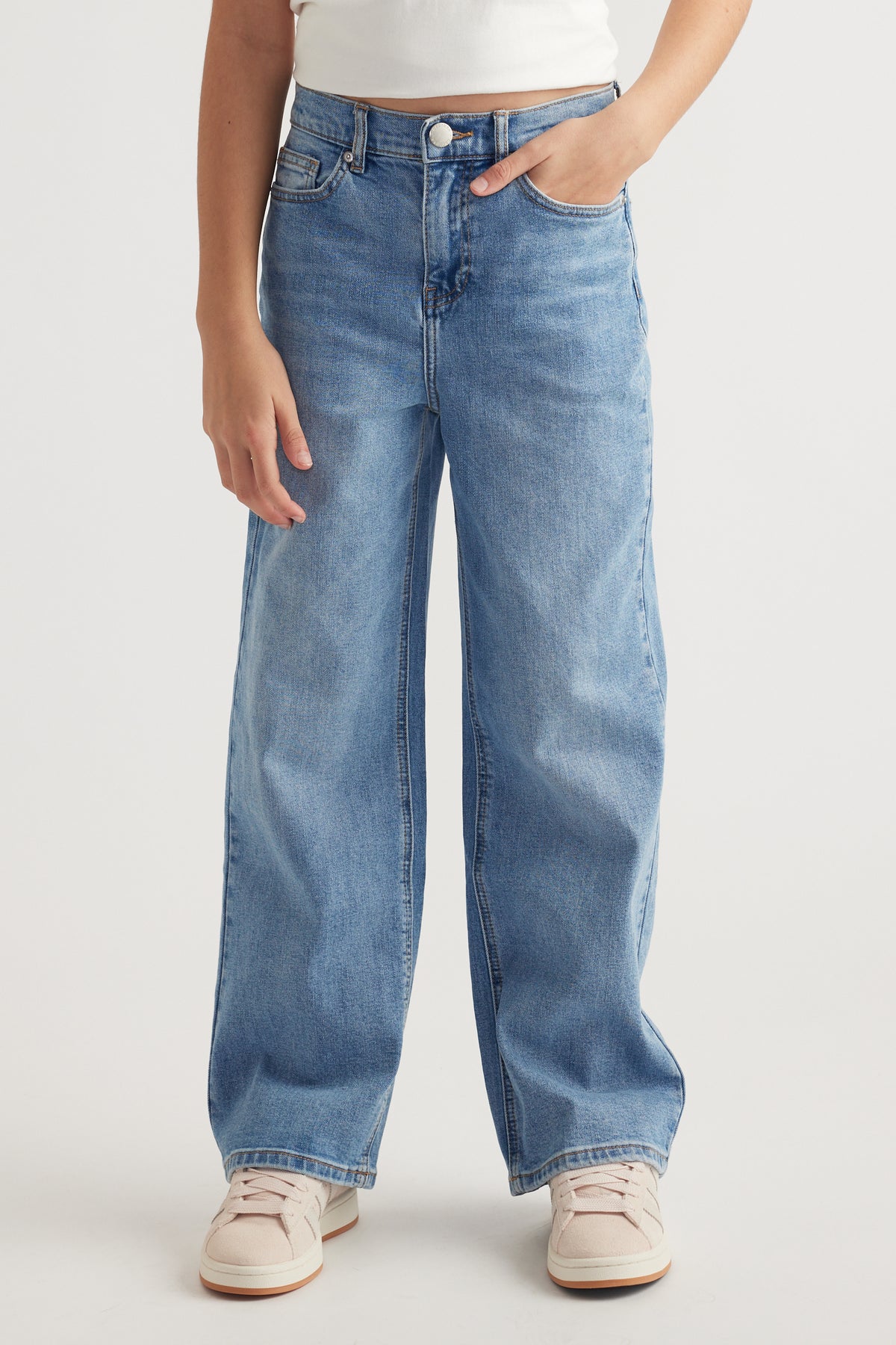 Front view of girl wearing mid-rise relaxed fit light blue jeans with functional pockets and white sneakers