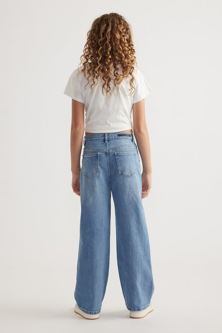 Rear view of girl wearing relaxed fit, mid-rise light blue jeans with functional back pockets and a white cropped tee