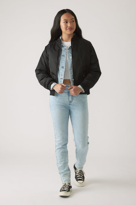 Teen girl wearing light wash skinny jeans layered with a denim jacket and black cropped bomber jacket with sneakers