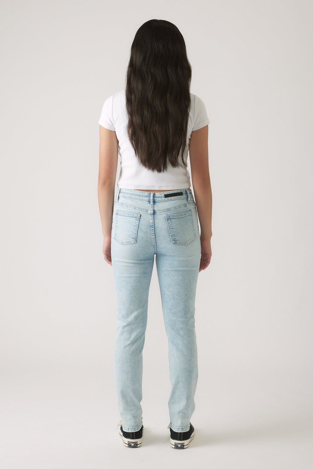Girl shown from behind wearing light wash skinny jeans and a fitted white short sleeve top with sneakers