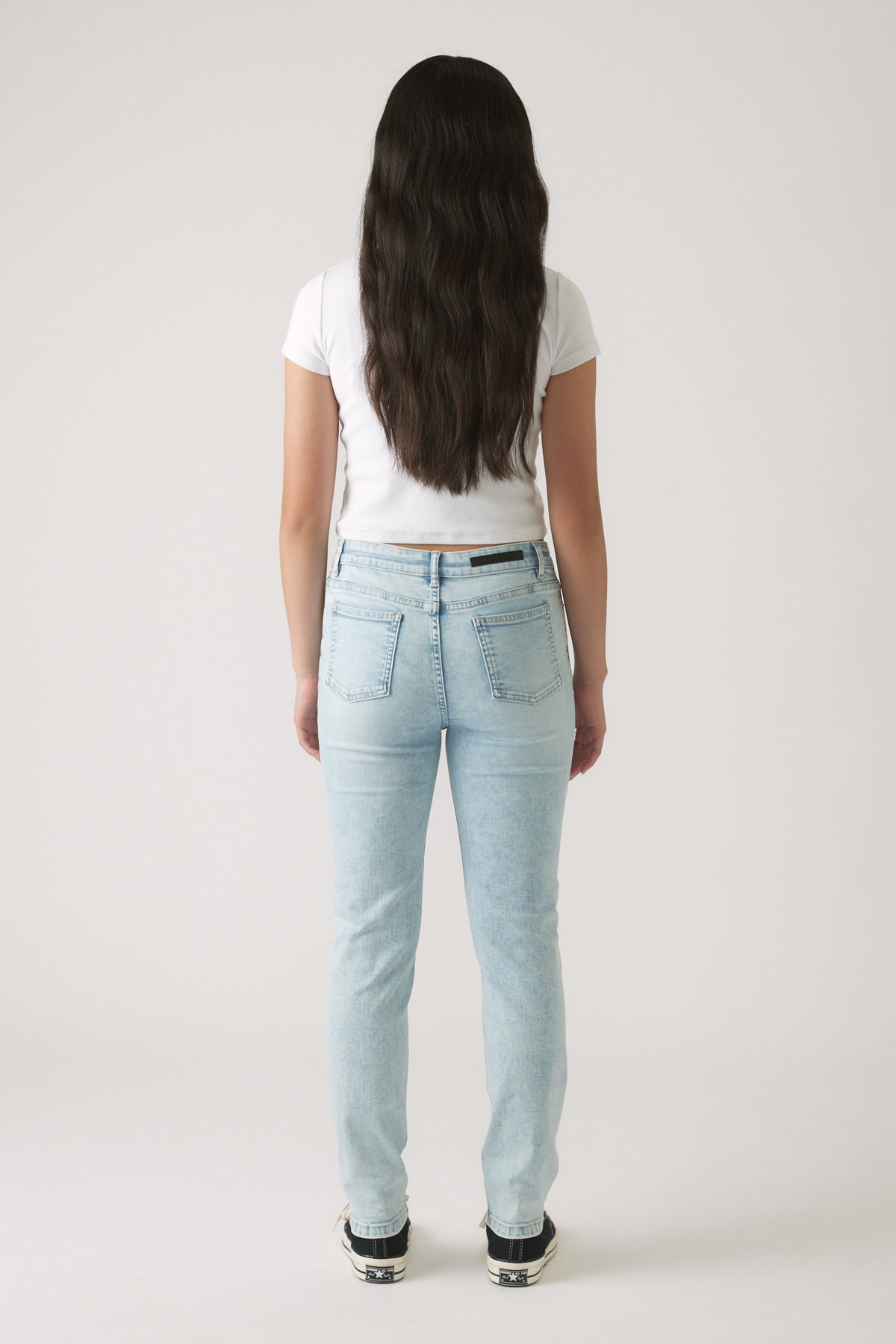 Girl shown from behind wearing light wash skinny jeans and a fitted white short sleeve top with sneakers