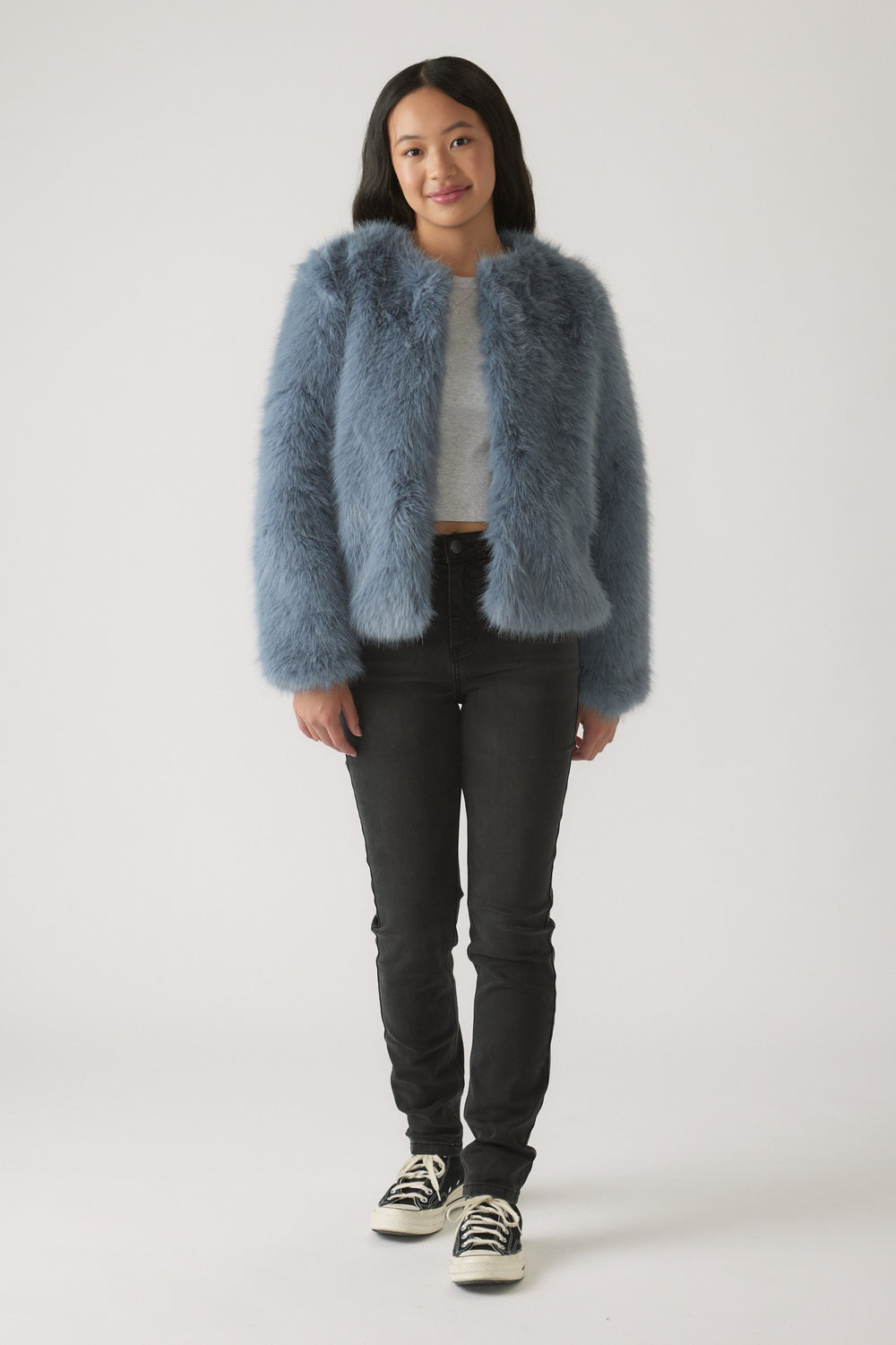 Girl wearing a soft blue fuzzy jacket over a light grey top with slim black jeans and black sneakers
