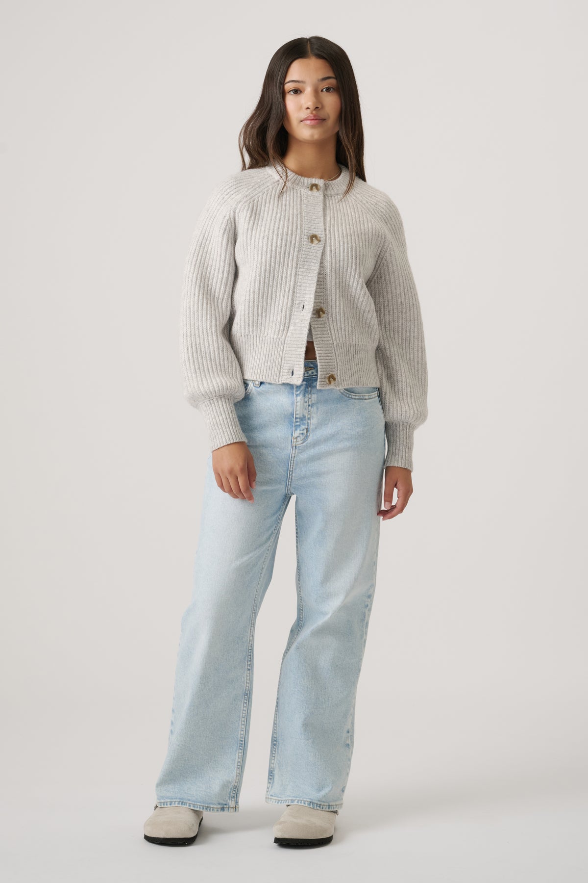Teen girl wearing a light grey button-up ribbed cardigan with balloon sleeves paired with relaxed light blue denim jeans
