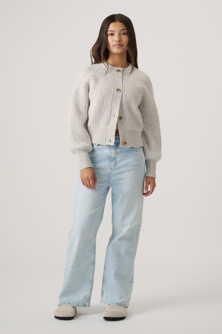 Teen girl wearing a light grey button-up ribbed cardigan with balloon sleeves paired with relaxed light blue denim jeans