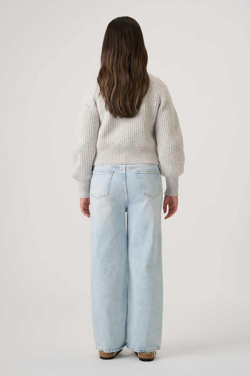 Back view of girl wearing a soft grey knit cardigan paired with relaxed wide-leg light blue denim jeans