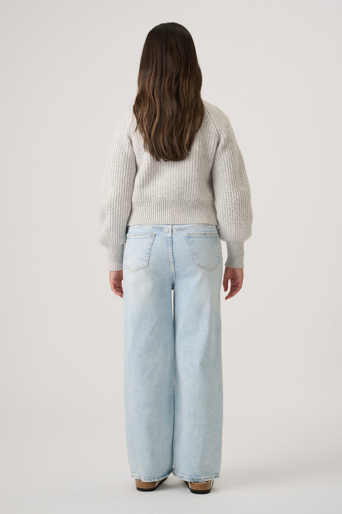 Back view of girl wearing a soft grey knit cardigan paired with relaxed wide-leg light blue denim jeans