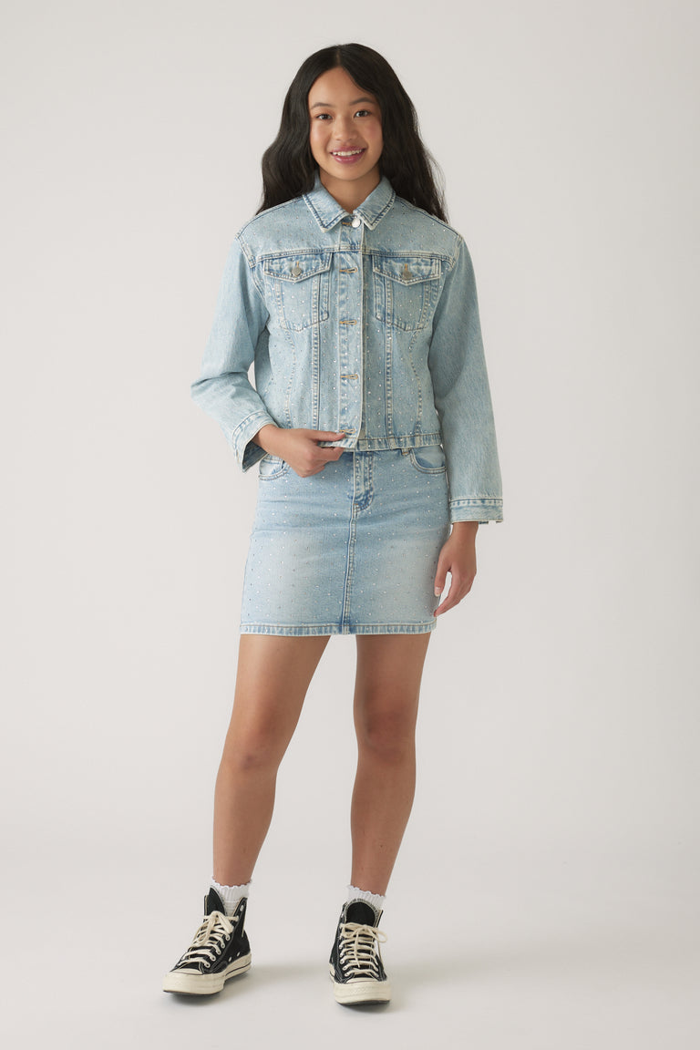 Teen girl wearing light wash denim jacket and embellished denim skirt paired with high-top sneakers and white socks