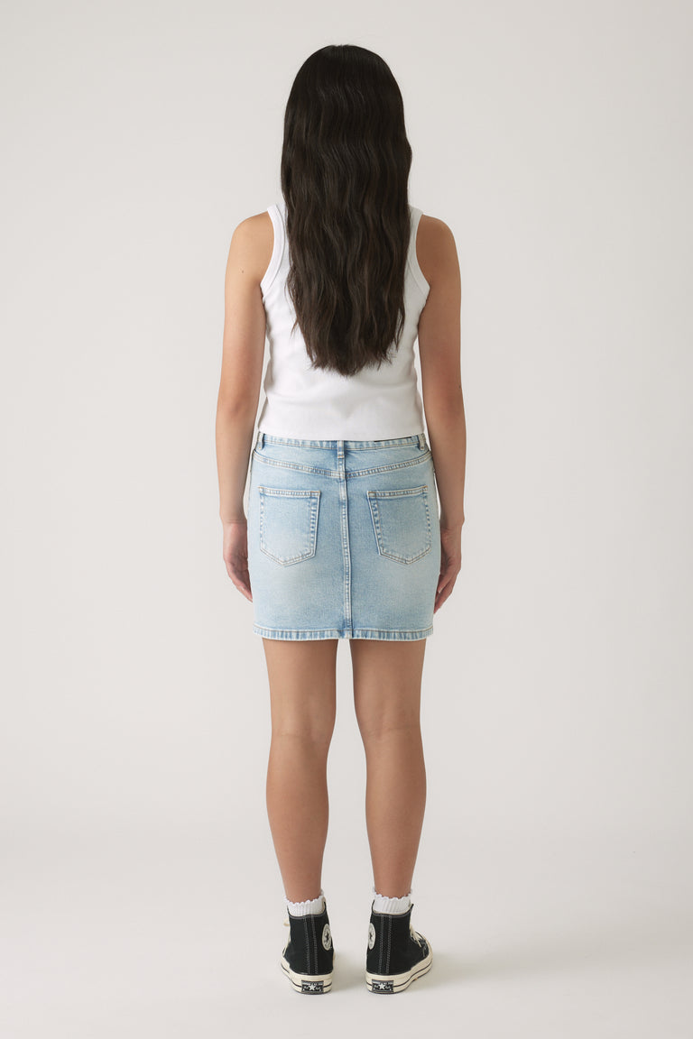 Girl wearing a light wash denim skirt paired with a sleeveless white top and black high-top sneakers, back view.
