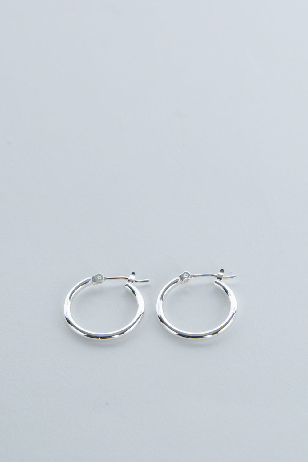 Pair of simple polished silver hoop earrings for girls with secure latch-back closures on soft gray background