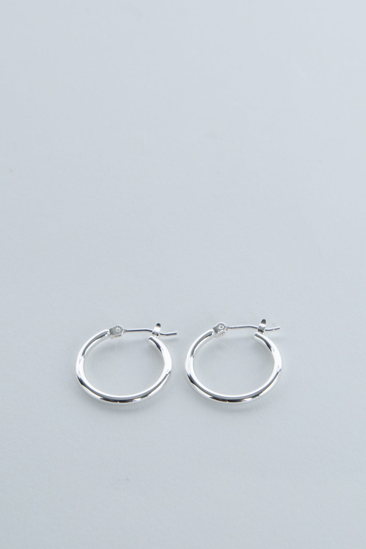 Pair of simple polished silver hoop earrings for girls with secure latch-back closures on soft gray background