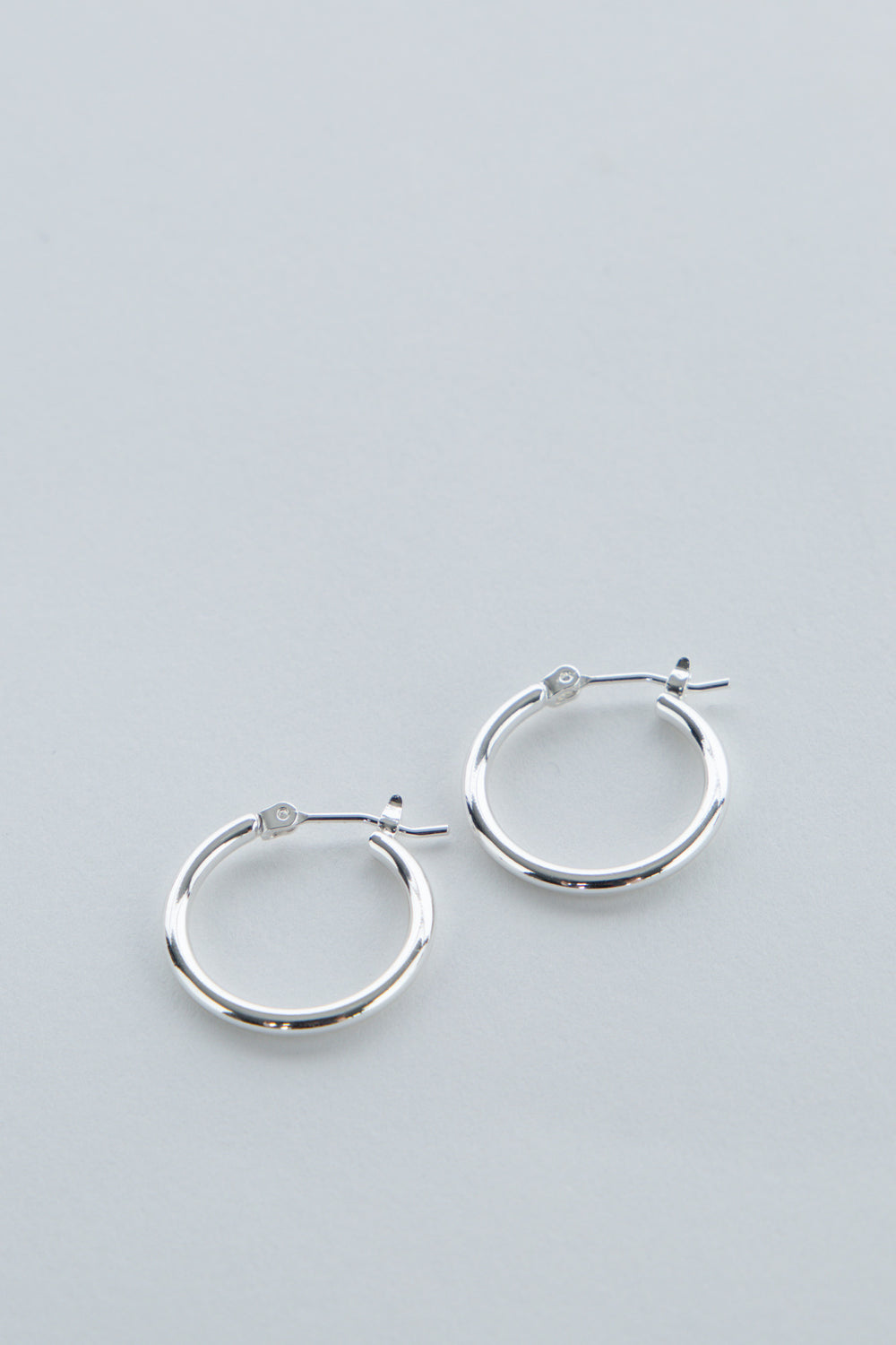 Pair of simple polished silver hoop earrings for girls with secure latch backs on light gray background