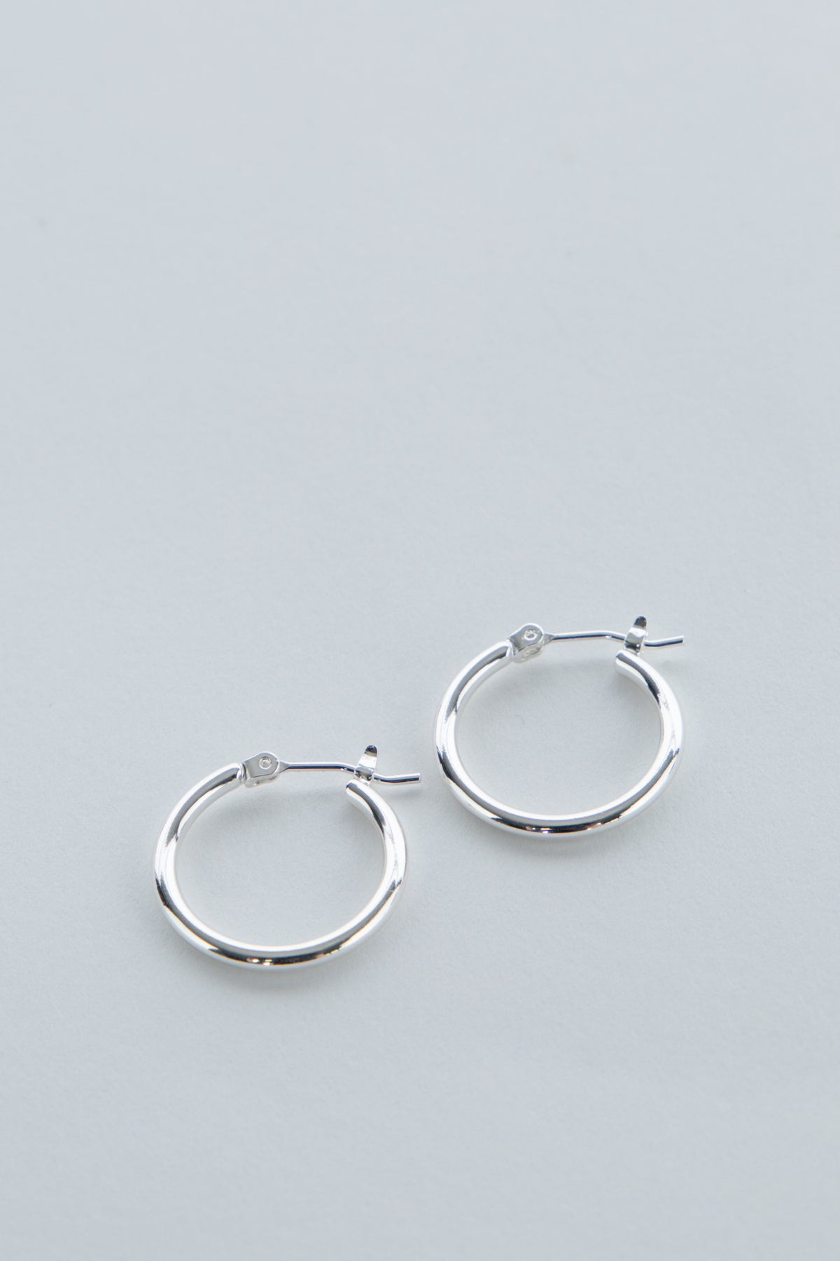 Pair of simple polished silver hoop earrings for girls with secure latch backs on light gray background
