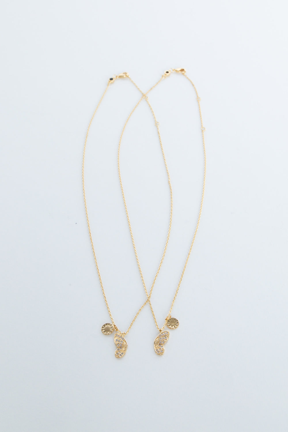 Two delicate gold necklaces featuring butterfly and sun-shaped charms laid flat on a white background