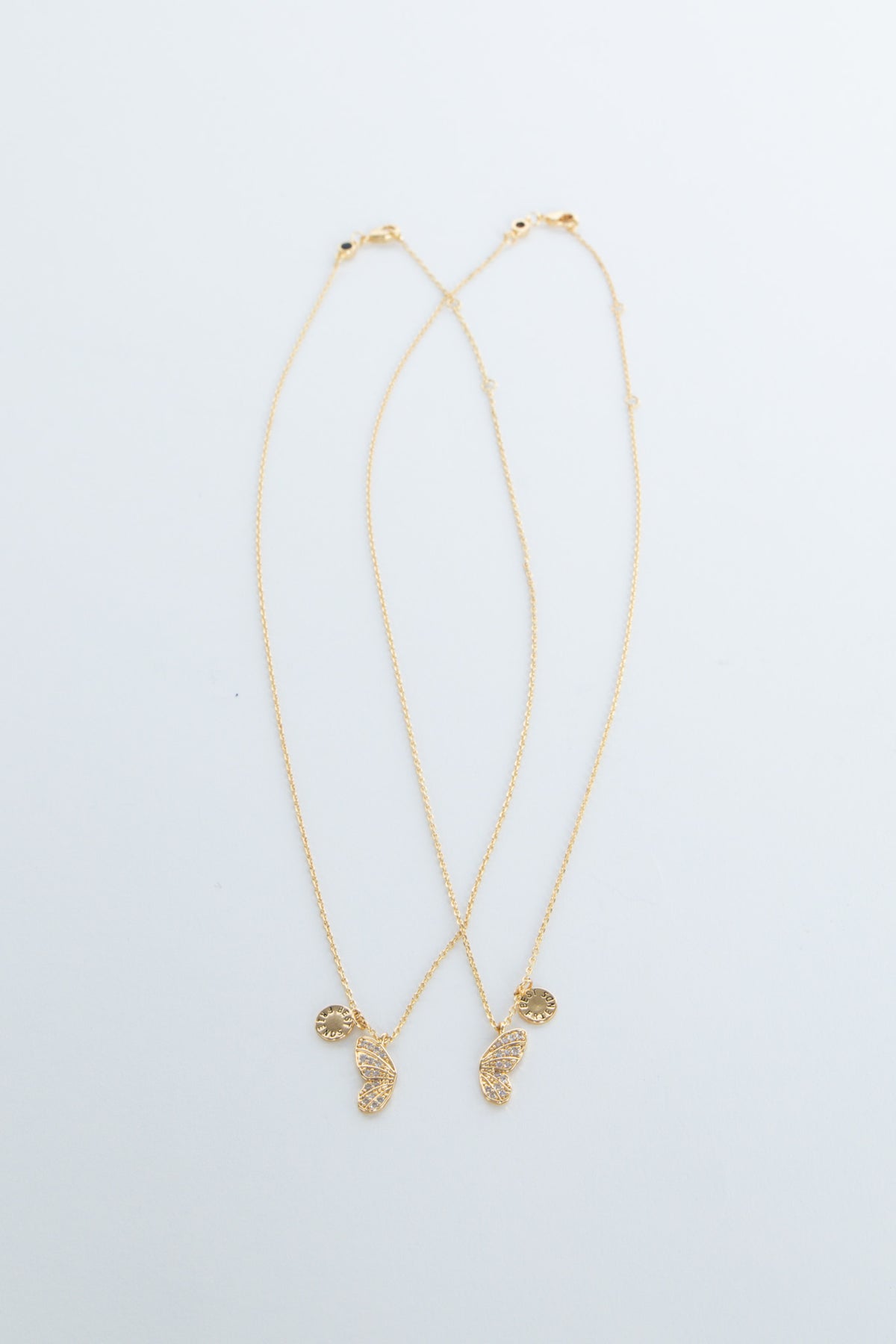 Two delicate gold necklaces featuring butterfly and sun-shaped charms laid flat on a white background