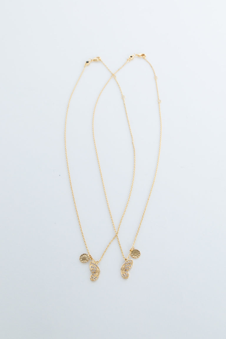 Two delicate gold necklaces featuring butterfly and sun-shaped charms laid flat on a white background