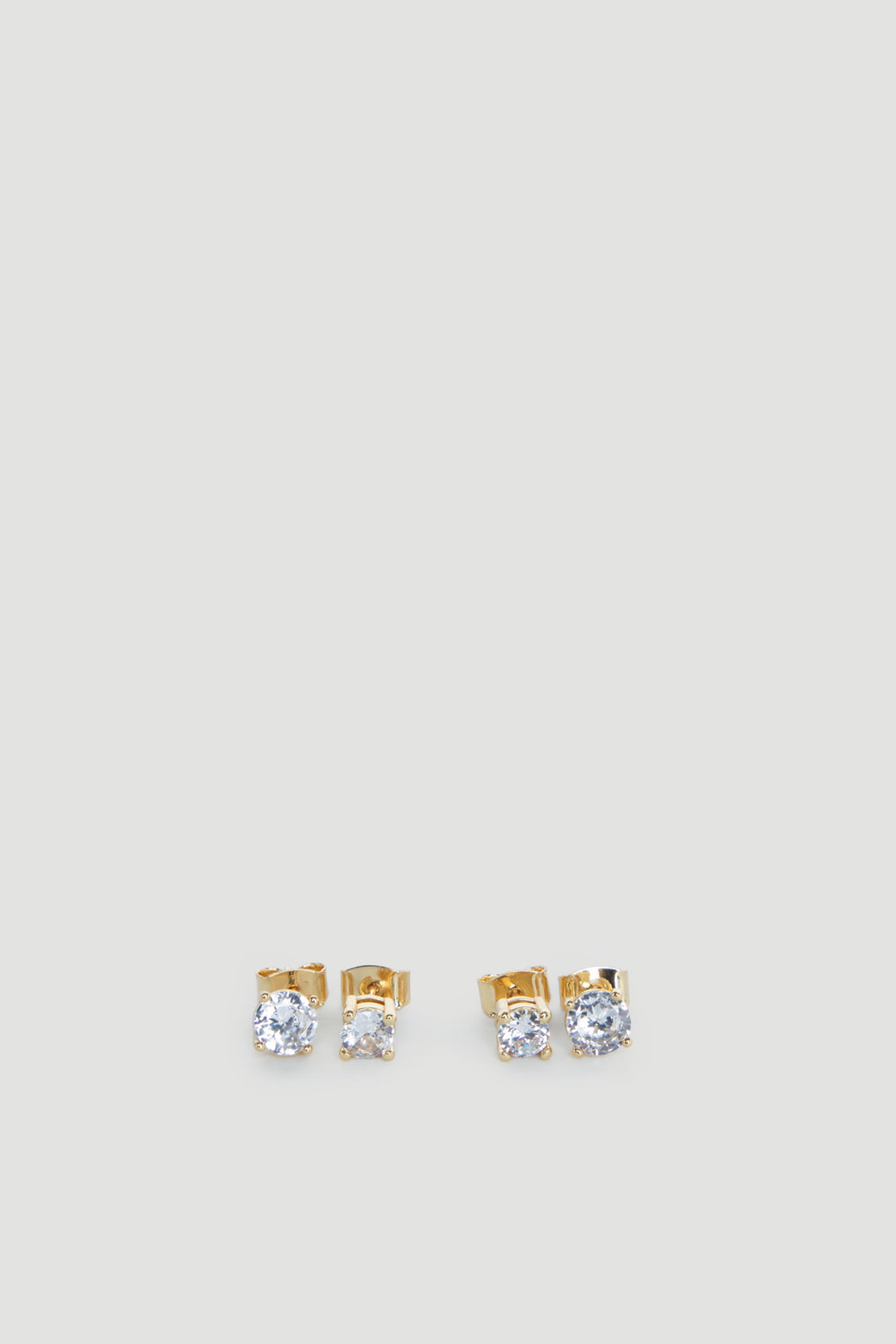 Two pairs of delicate gold stud earrings each featuring sparkling clear stones on a light grey background
