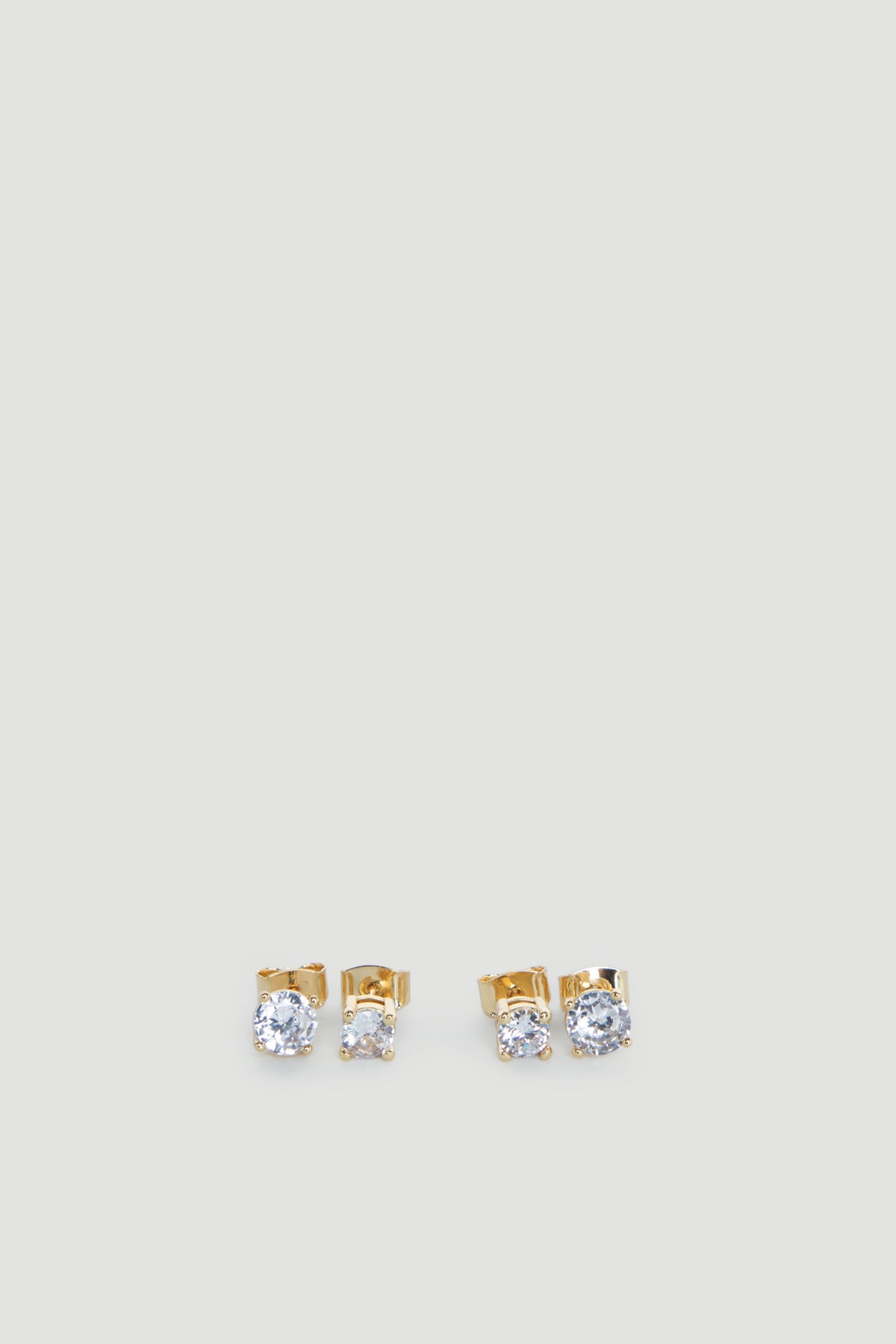 Two pairs of delicate gold stud earrings each featuring sparkling clear stones on a light grey background