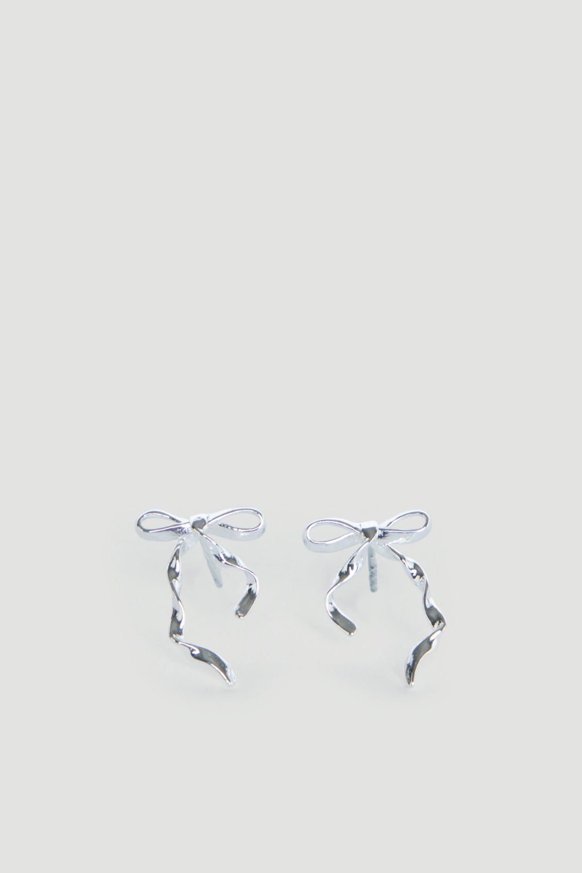 Delicate silver bow-shaped stud earrings with flowing ribbon details, designed for girls with a charming, graceful touch.