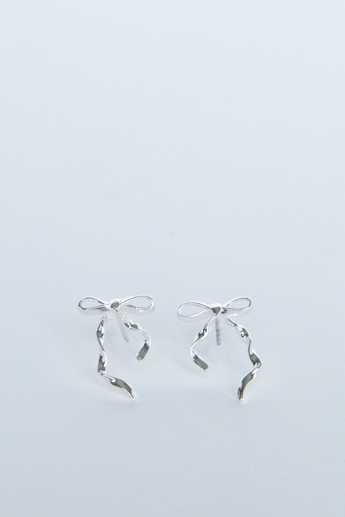 Delicate silver bow-shaped stud earrings with flowing ribbon details, perfect for adding a subtle touch of elegance.