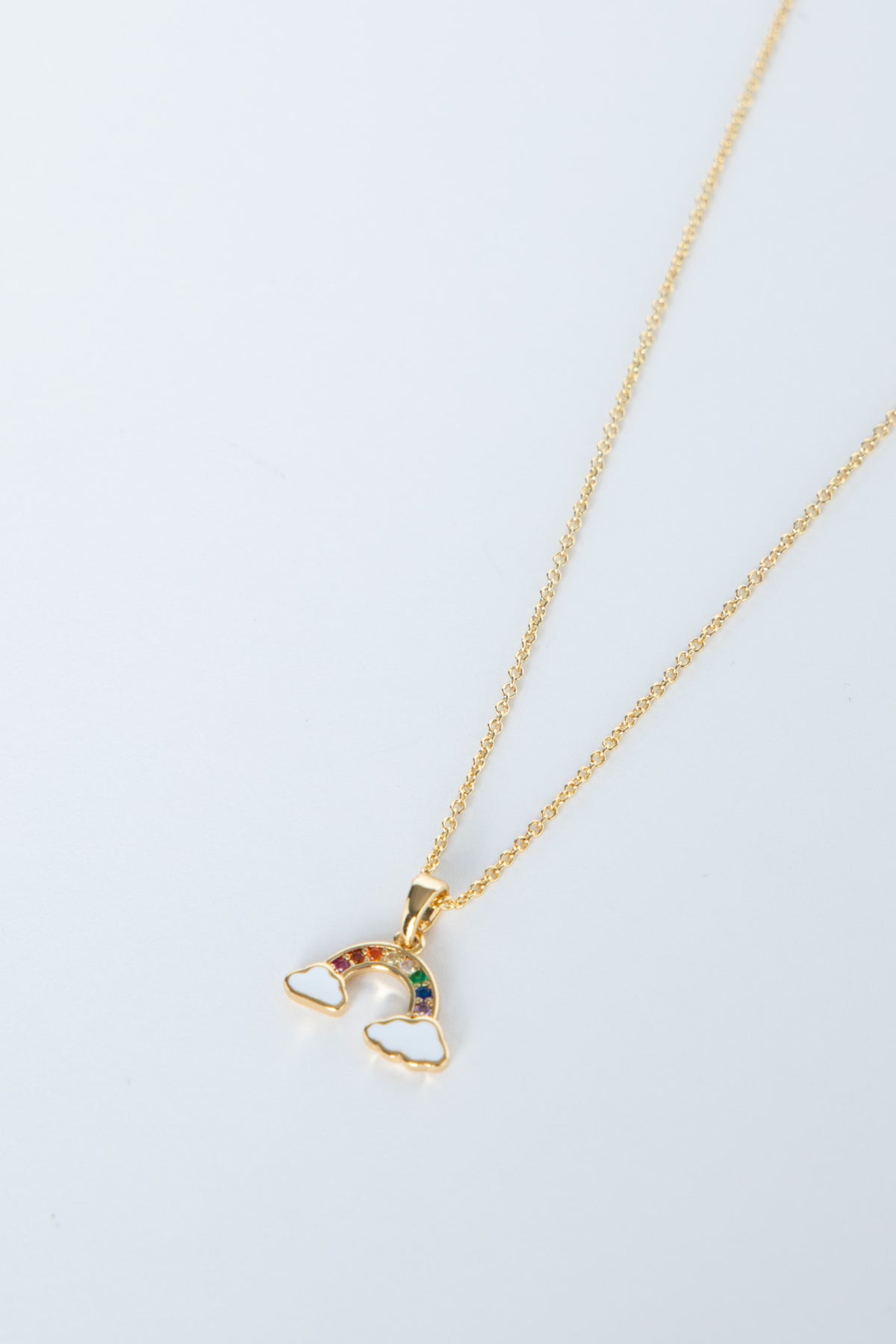 Delicate gold necklace featuring a small rainbow pendant with colorful stones and cloud accents on a fine chain