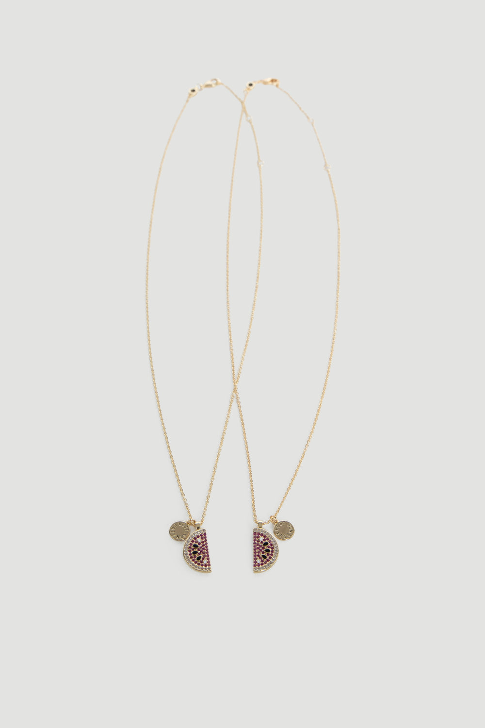 Two delicate gold chains featuring watermelon-inspired pendants with pink and green stones on a neutral background