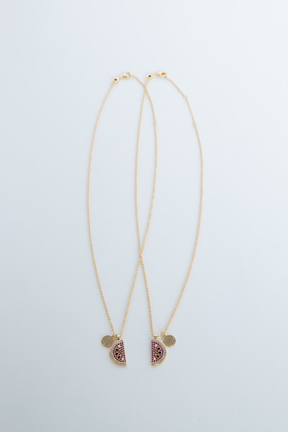 Two delicate 9ct gold necklaces with watermelon-shaped pendants adorned with pink and green stones on thin chains.