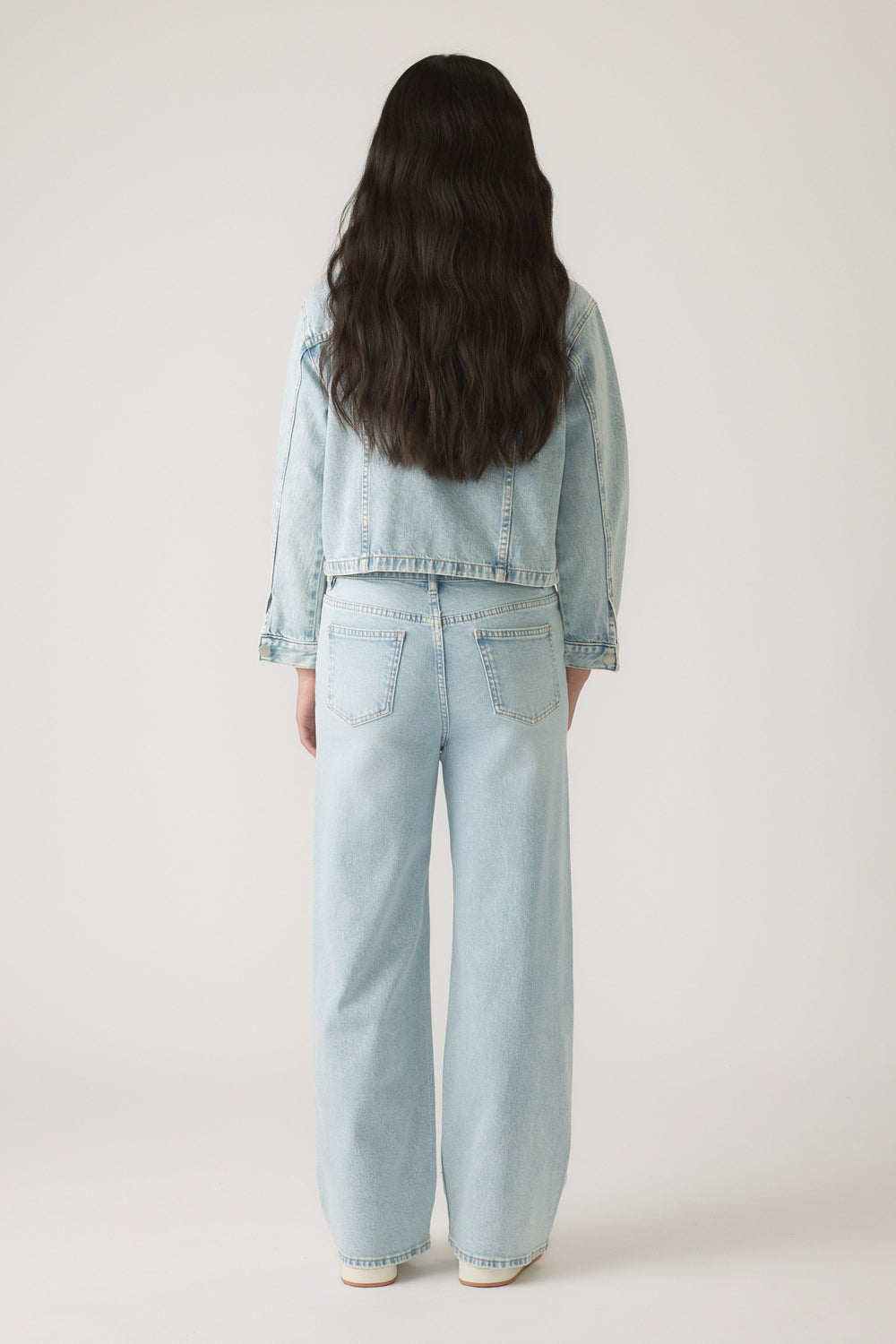 Girl shown from behind wearing a light wash Girls Embellished Denim Jacket with matching wide-leg jeans by DECJUBA.