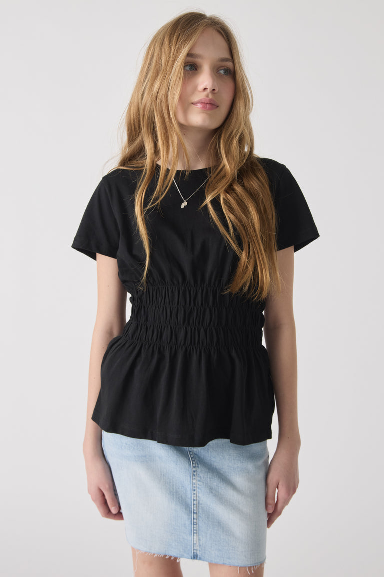 Girl wearing a black smocked waist tee paired with a light denim skirt, styled for casual everyday comfort.