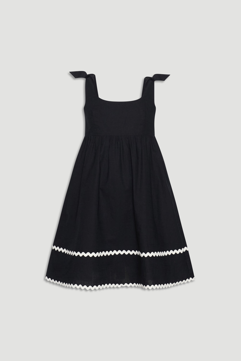 Black sleeveless girls mini dress with square neckline, tie shoulder straps, and white wavy trim near hem.