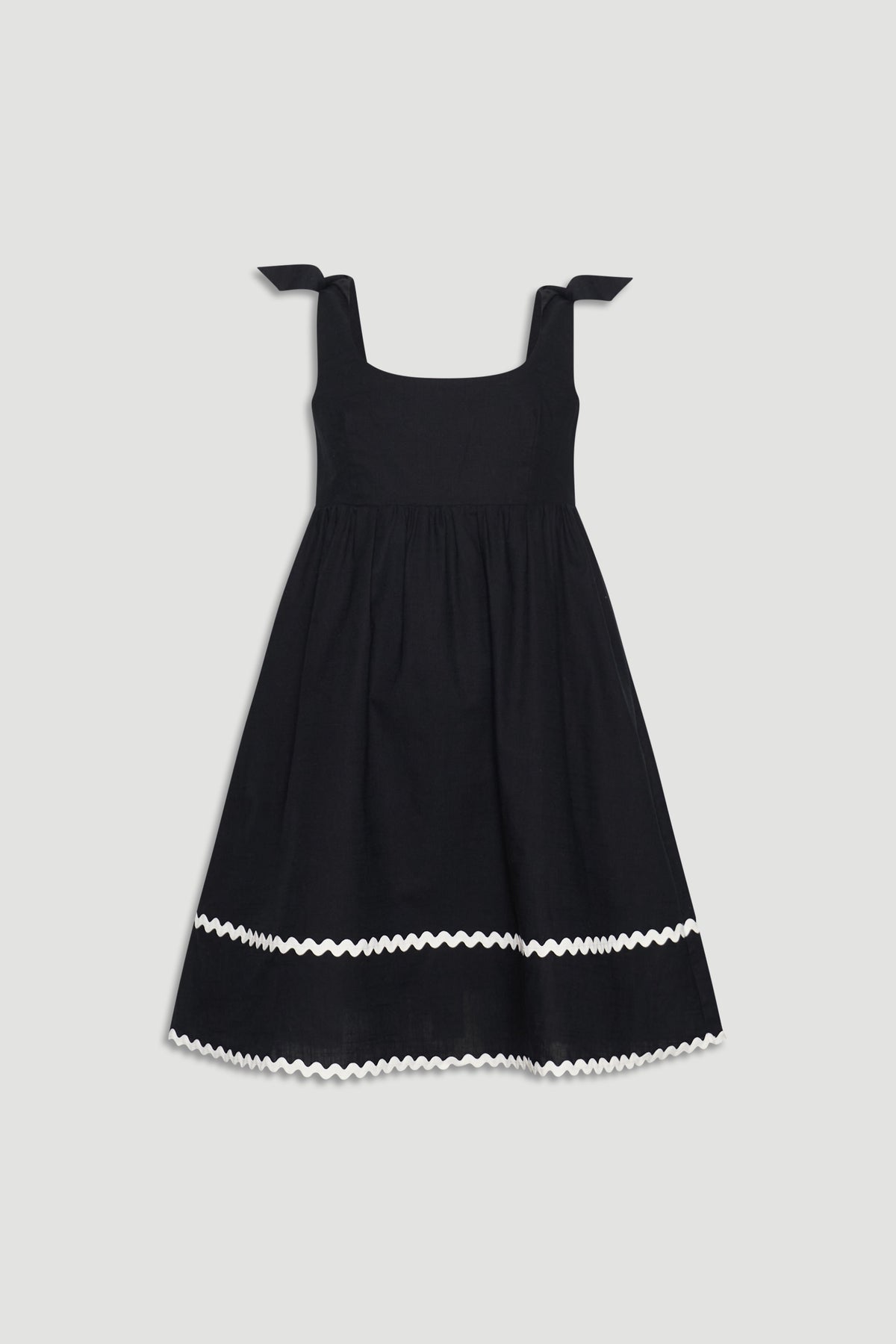 Black sleeveless girls mini dress with square neckline, tie shoulder straps, and white wavy trim near hem.