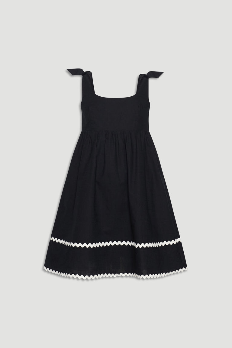Black sleeveless girls mini dress with square neckline, tie shoulder straps, and white wavy trim near hem.