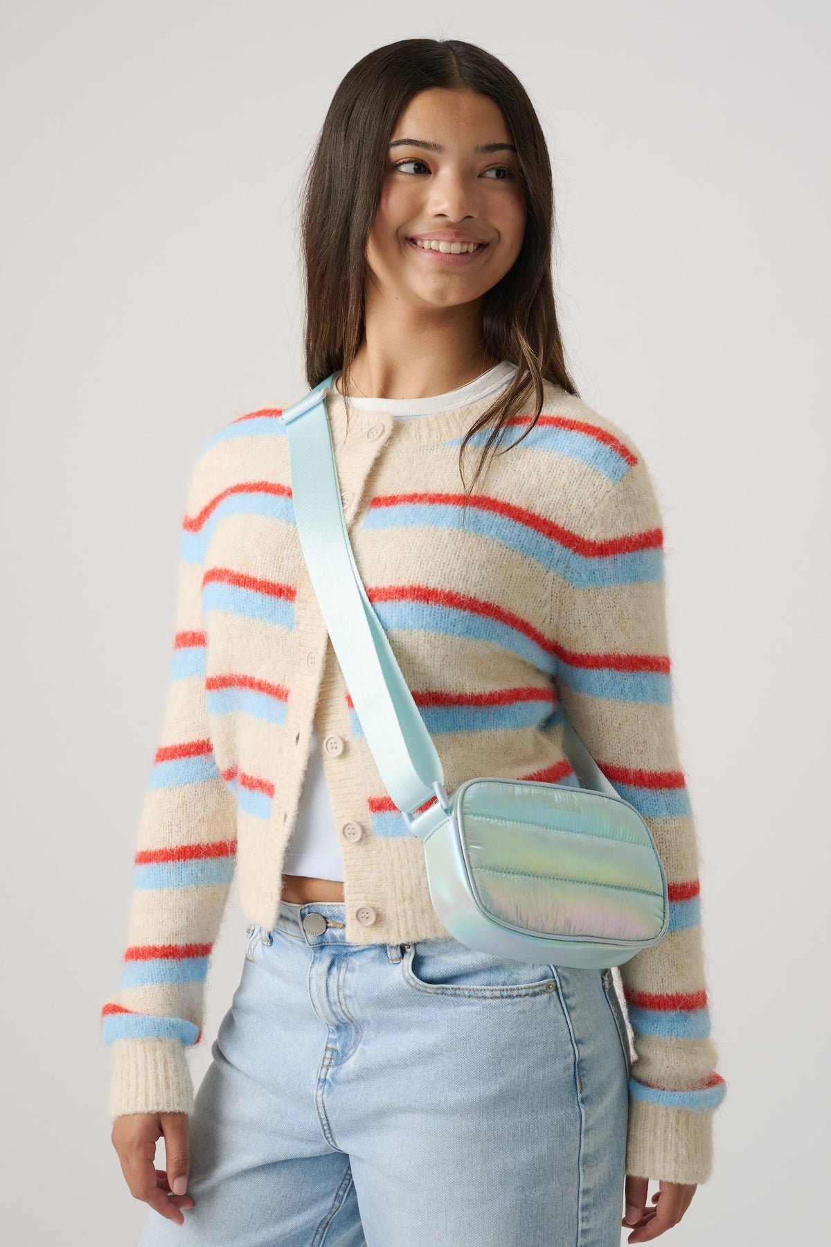 Girl wearing a striped fuzzy cardigan paired with light blue jeans and a pastel padded crossbody bag for a casual look.