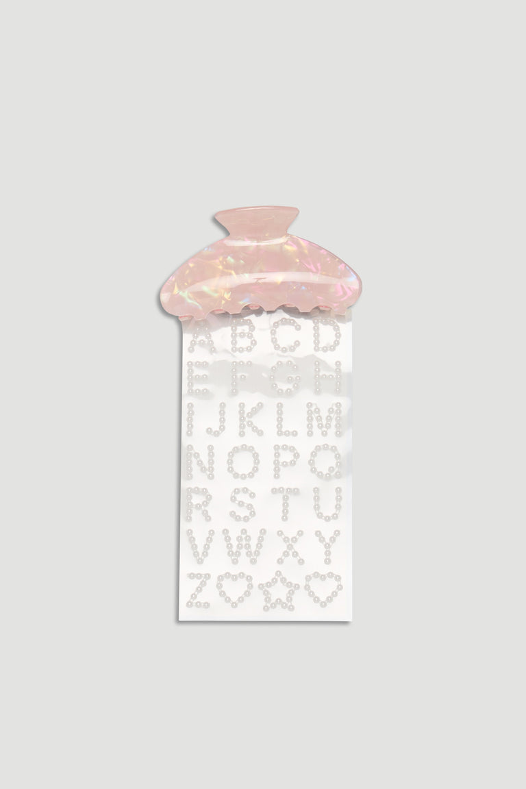Pink iridescent hair claw clip paired with pearl-studded alphabet and shape stickers for customization.