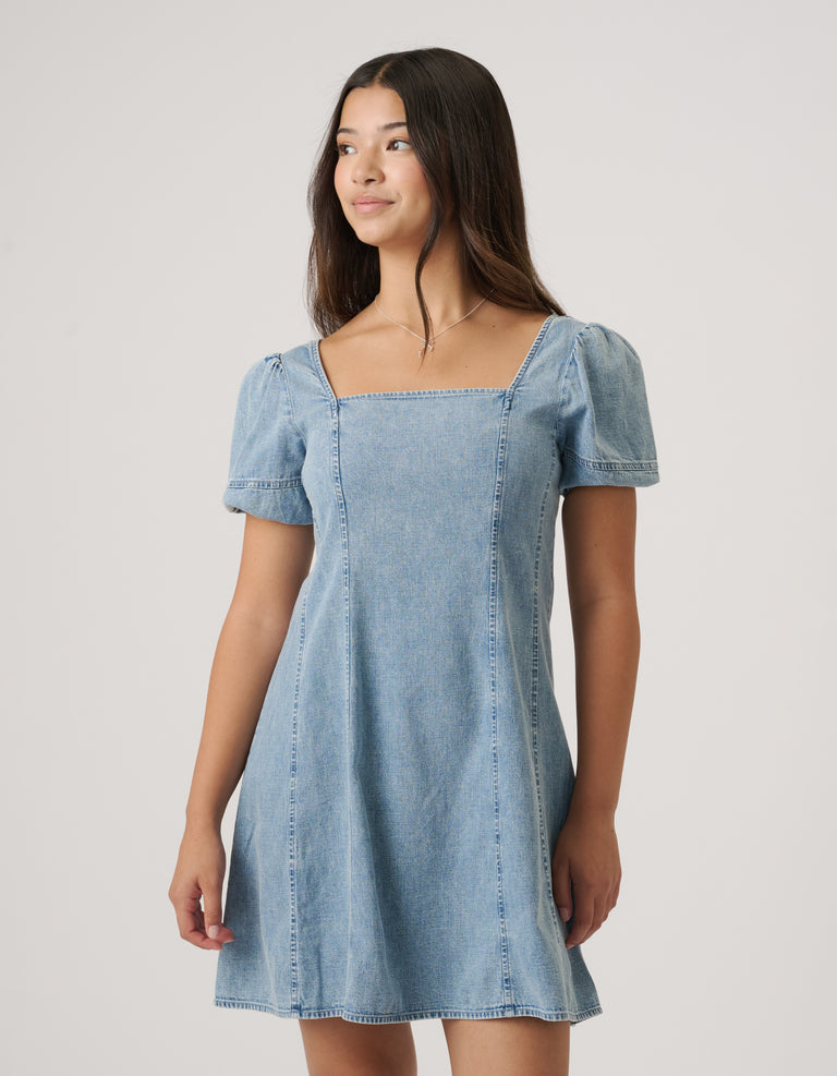 Girl wearing a light wash denim mini dress with puffed short sleeves and a square neckline, styled simply for everyday wear.