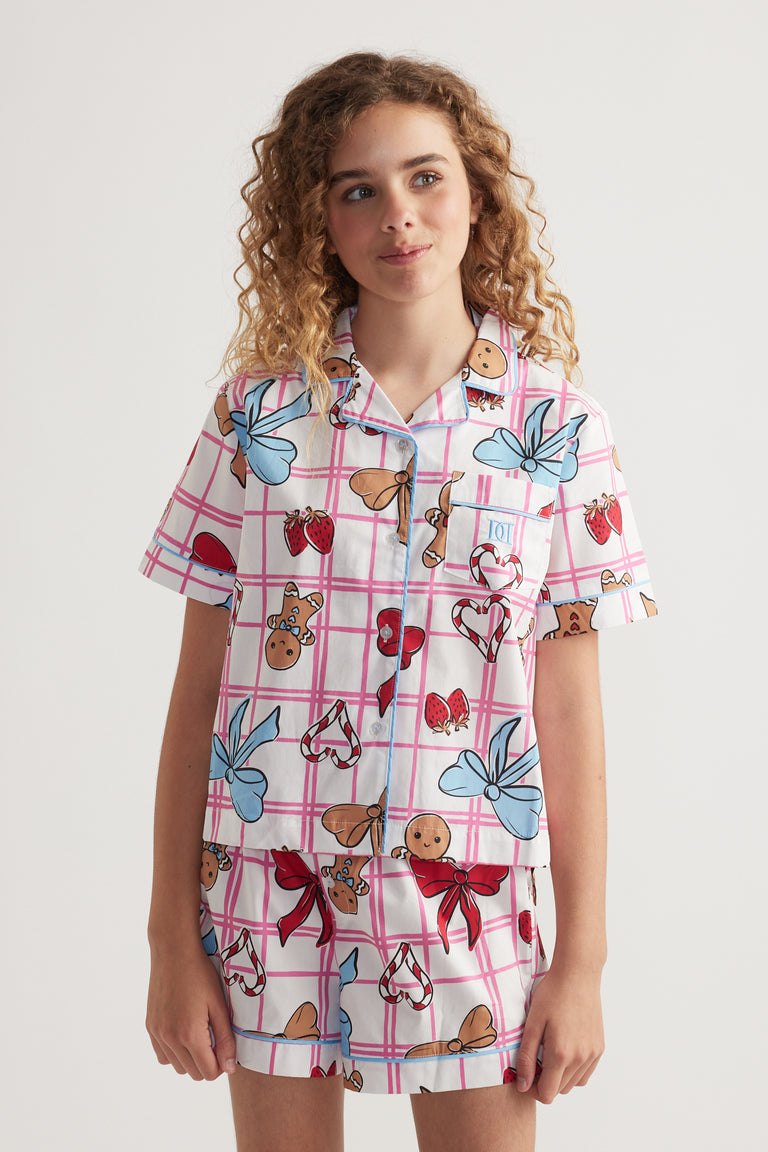 Girl wearing a pink plaid sleep set with a collared short sleeve shirt and matching printed shorts