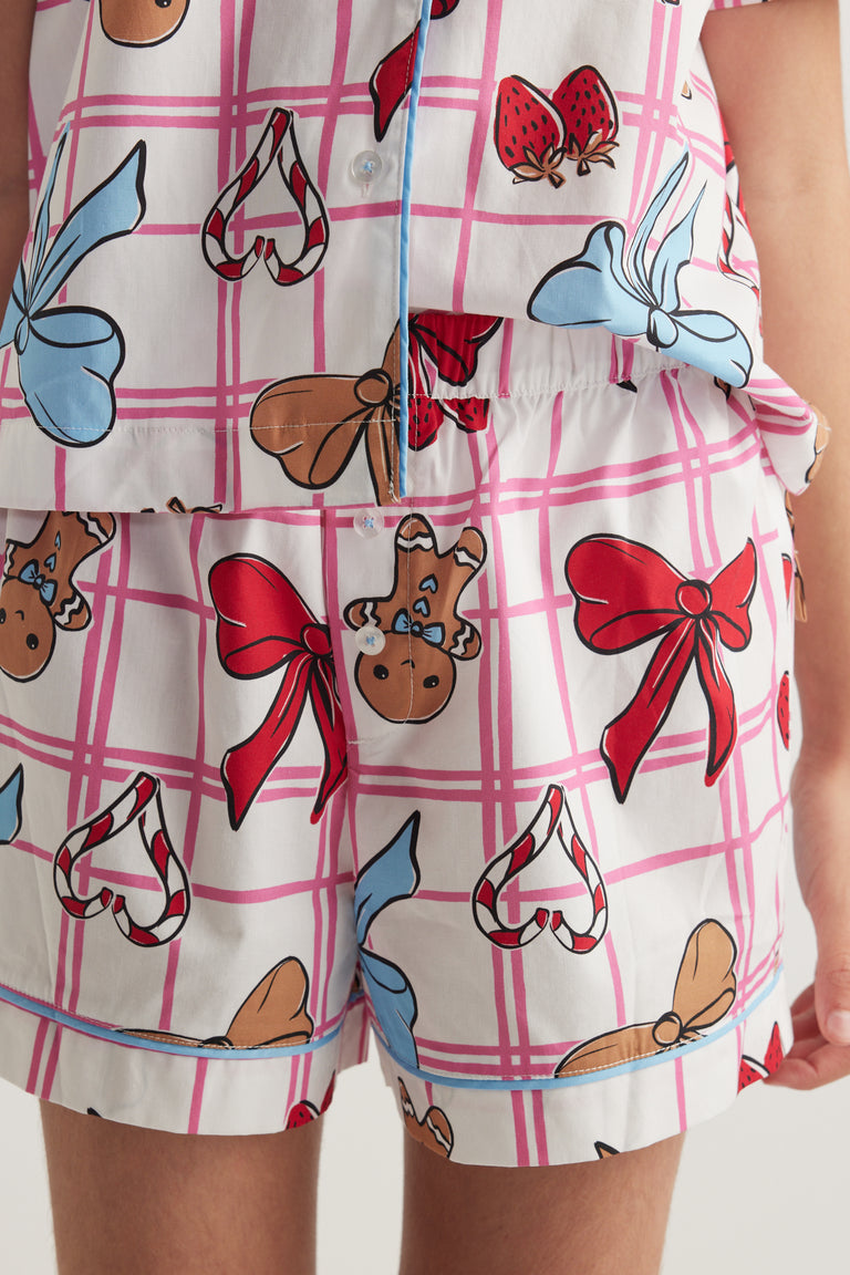Girls pink checked sleep set with a collared button-up shirt and matching shorts decorated with bows and festive prints