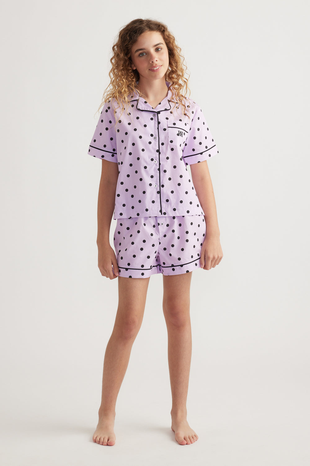 Girl wearing a lilac polka dot sleep set with a collared shirt and matching elastic waist shorts