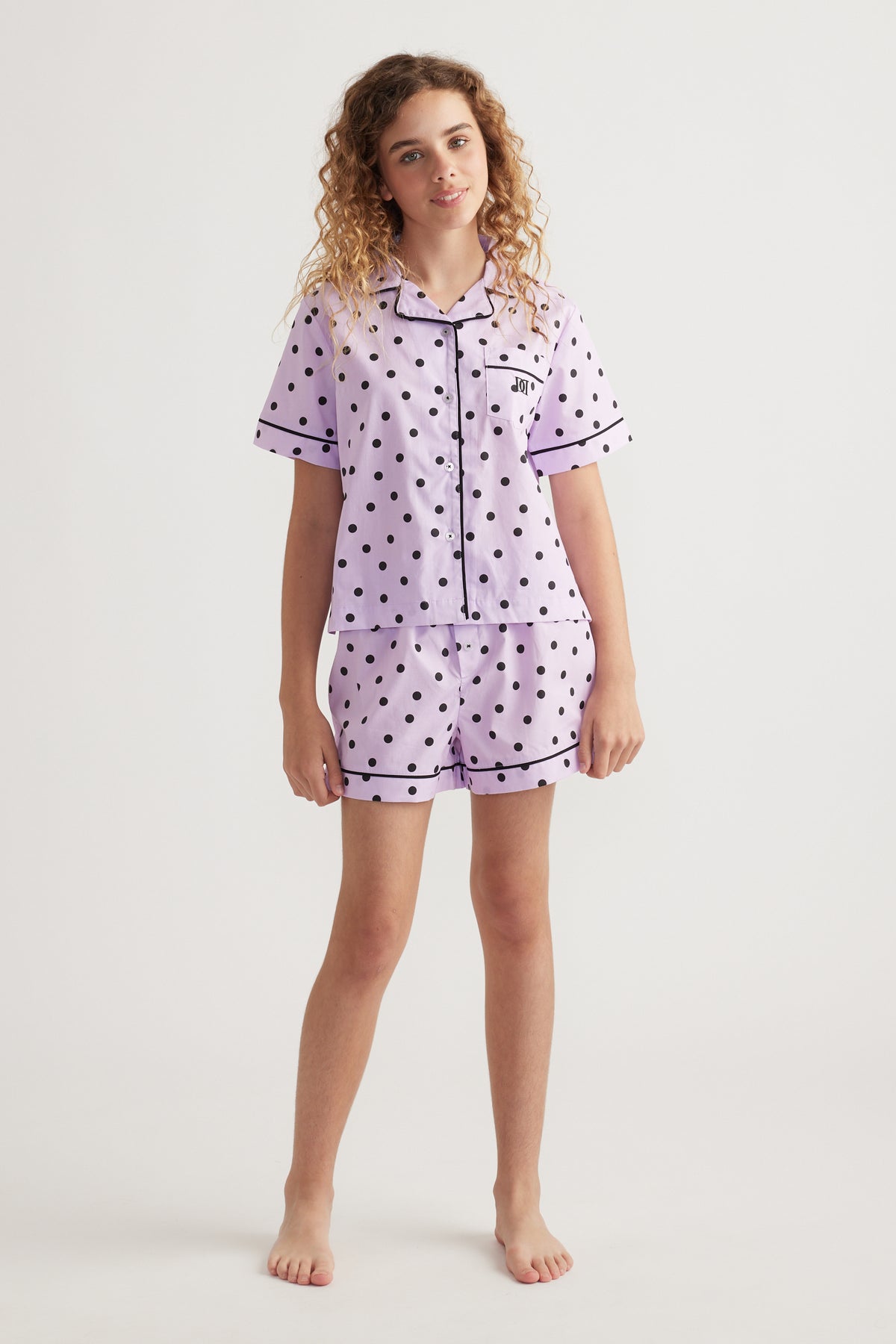 Girl wearing a lilac polka dot sleep set with a collared shirt and matching elastic waist shorts