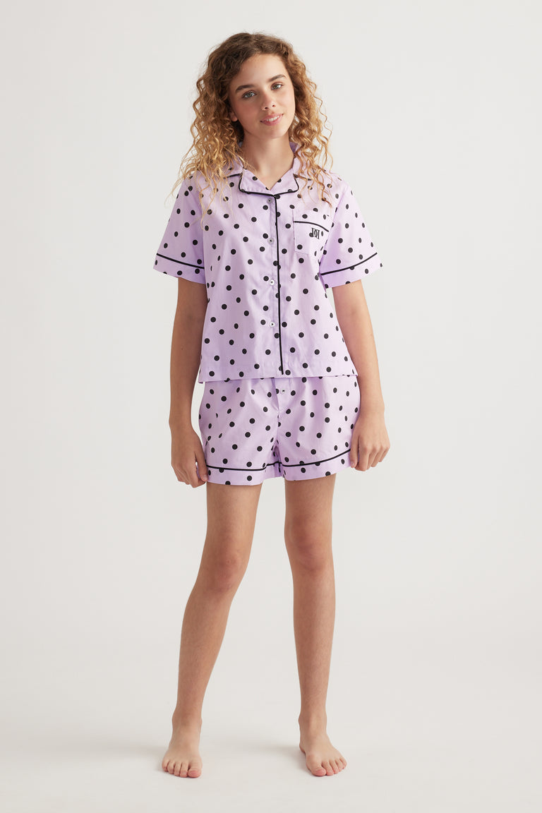 Girl wearing a lilac polka dot sleep set with a collared shirt and matching elastic waist shorts
