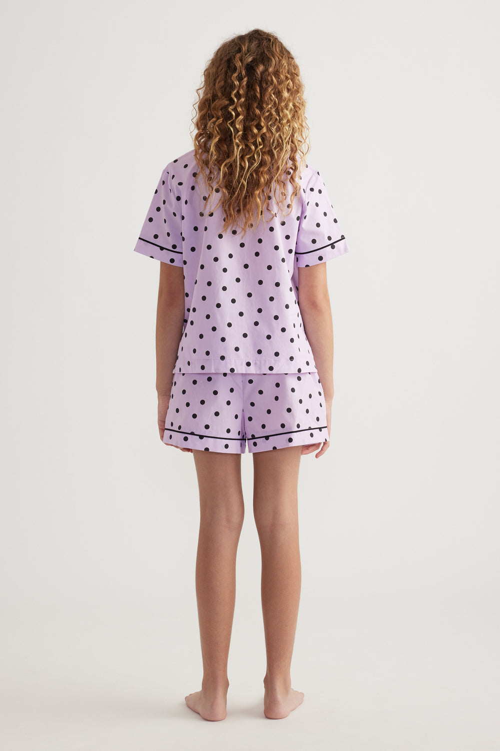 Back view of girl wearing a lilac polka dot sleep set with a short sleeve shirt and matching shorts