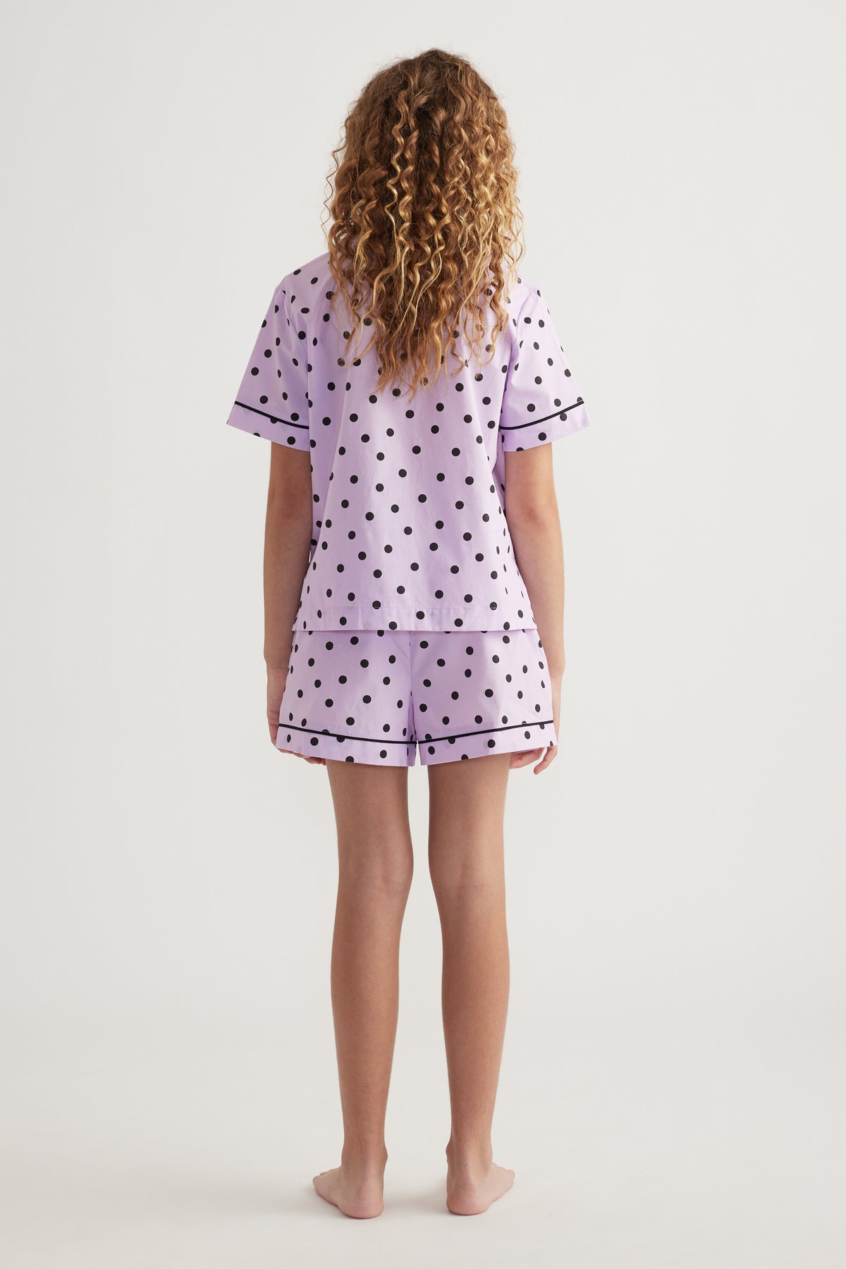 Back view of girl wearing a lilac polka dot sleep set with a short sleeve shirt and matching shorts